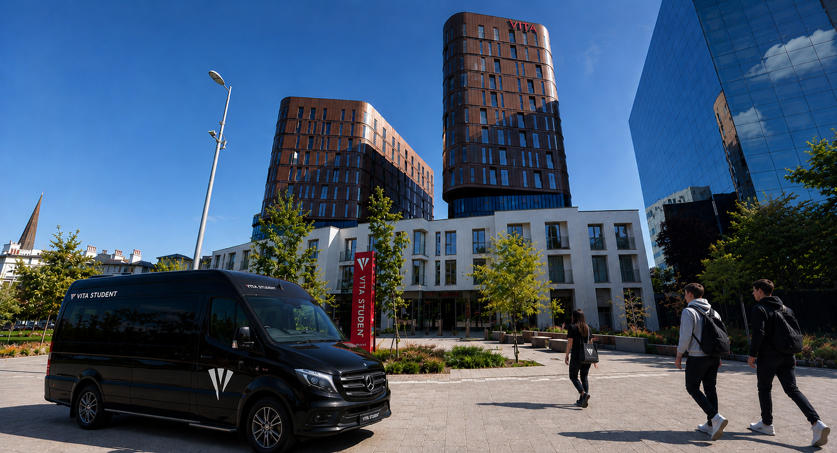 A black VITA Student van is parked in front of a modern student accommodation building in Coventry, with two tall towers, glass offices, trees, and people walking on a sunny day.