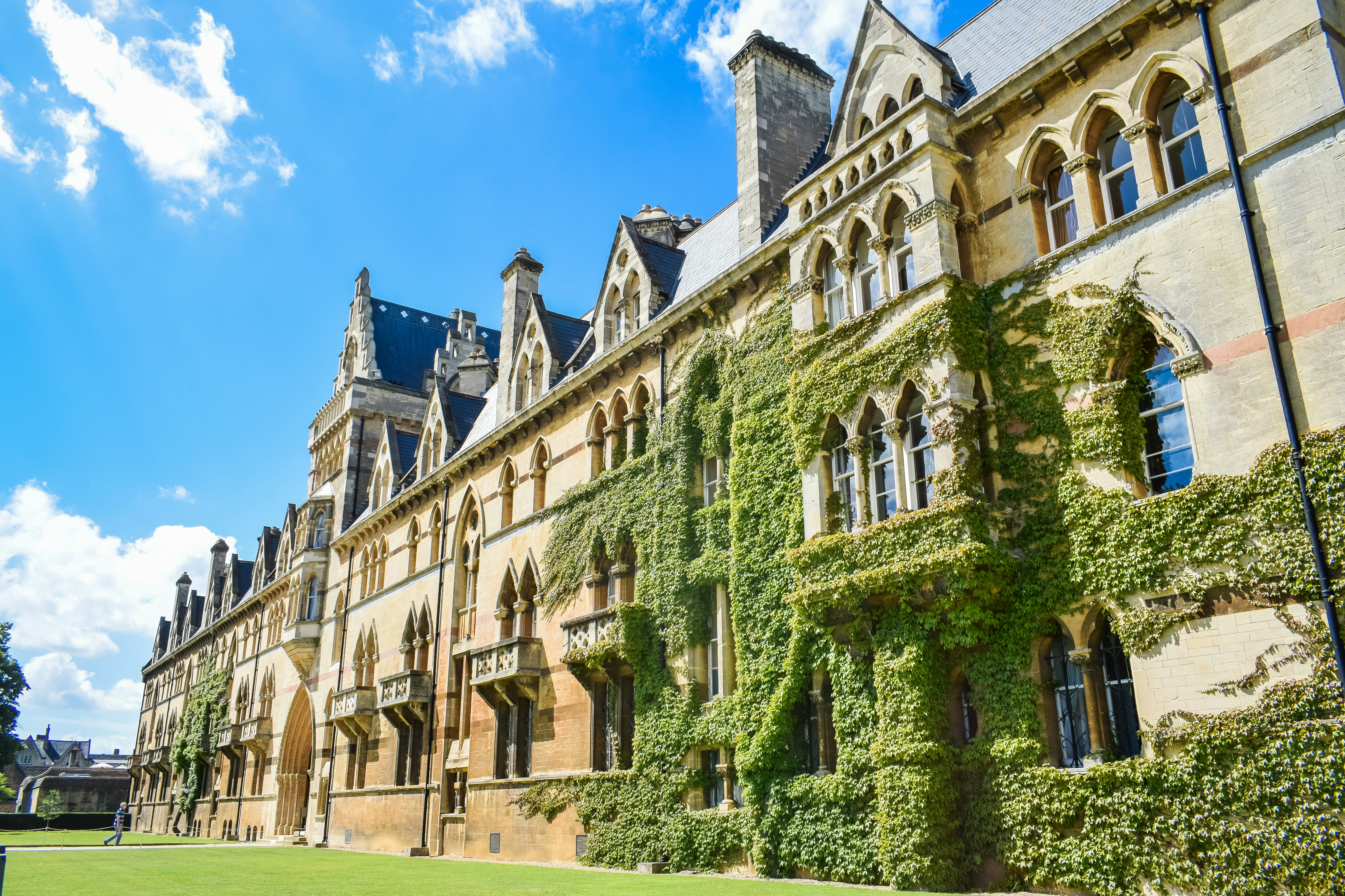 A historic stone building with arched windows and ivy on the facade stands beneath a bright blue sky. The well-kept green lawn in front highlights its prestige, reminiscent of institutions featured in the QS World University Rankings 2027.