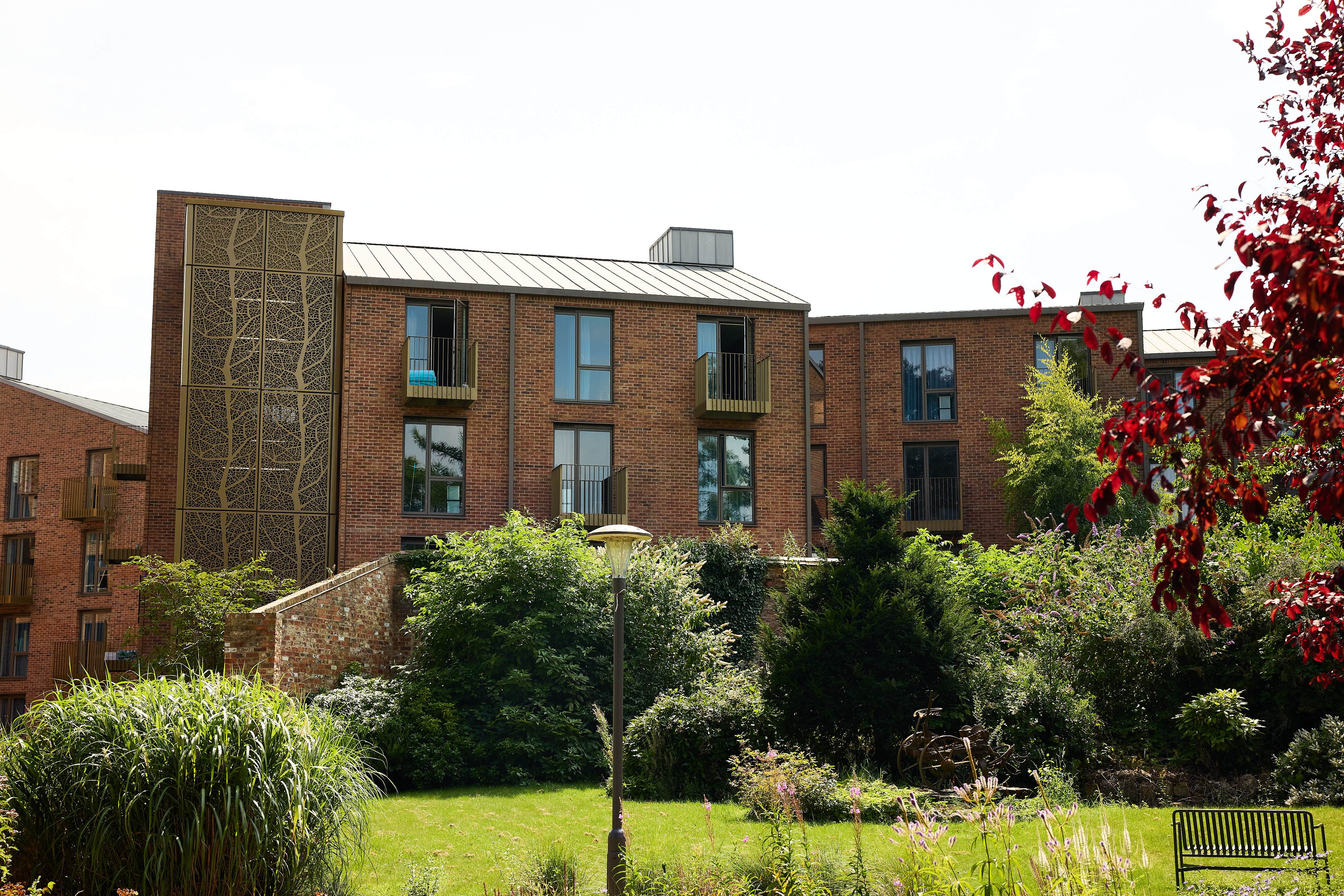 A modern brick apartment building with large windows and small balconies, Vita Student York is surrounded by lush greenery, trees, and a well-kept grassy garden under bright daylight.