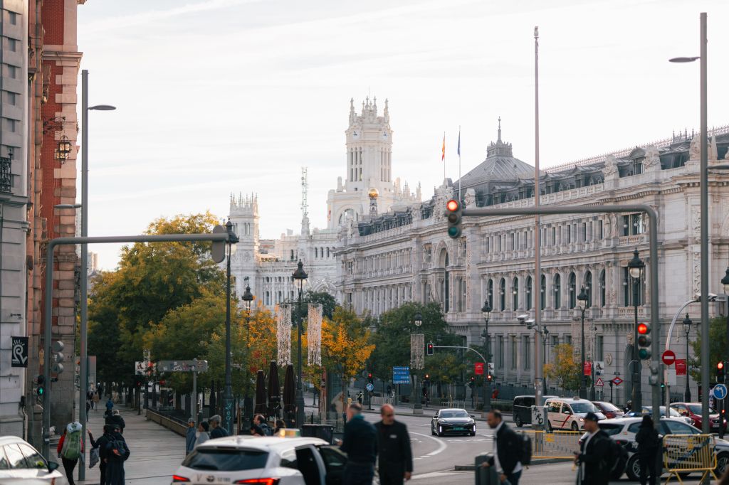 A busy city street in Madrid with cars, people walking, historic white buildings, and a tall tower in the background under a cloudy sky—perfect for those seeking things to do in Madrid or exploring student activities Madrid has to offer.