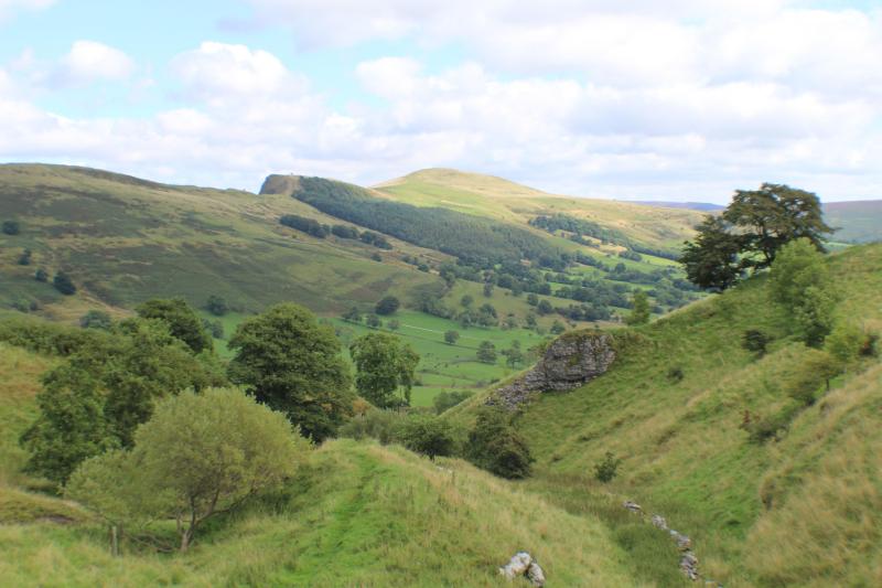 A scenic view of rolling green hills, scattered trees, and a partly cloudy sky, showcasing a peaceful countryside landscape perfect for students seeking relaxing day trips from Manchester.