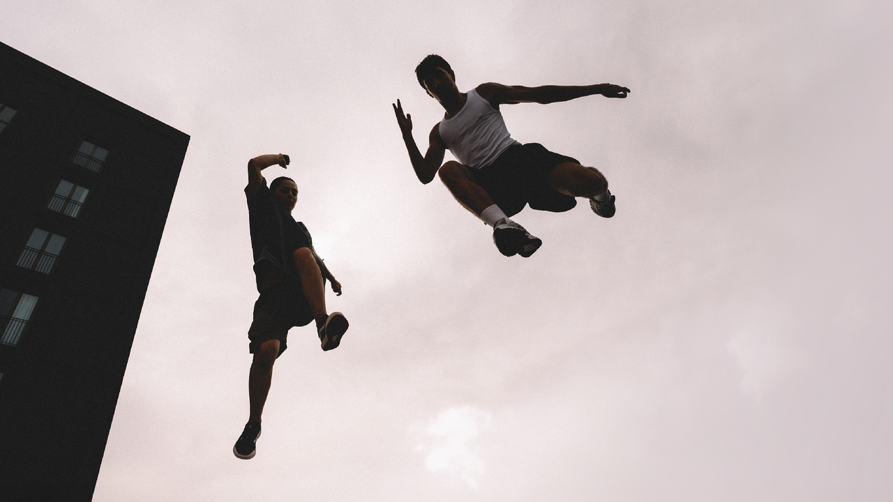 Two people are captured mid-air while jumping, with a dramatic sky in the background and part of a building visible on the left side of the image—possibly celebrating an exciting viewing booking planned for 2027.