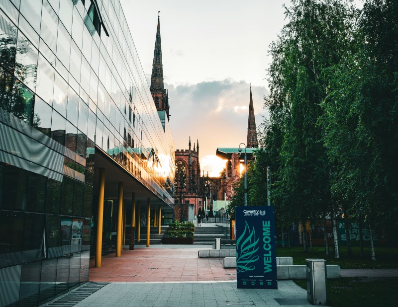 Modern glass building and welcome sign in front of historic cathedral with tall copper towers at sunset, trees lining one side, creating a blend of contemporary and historical architecture—an inviting spot for students seeking things to do in the city.