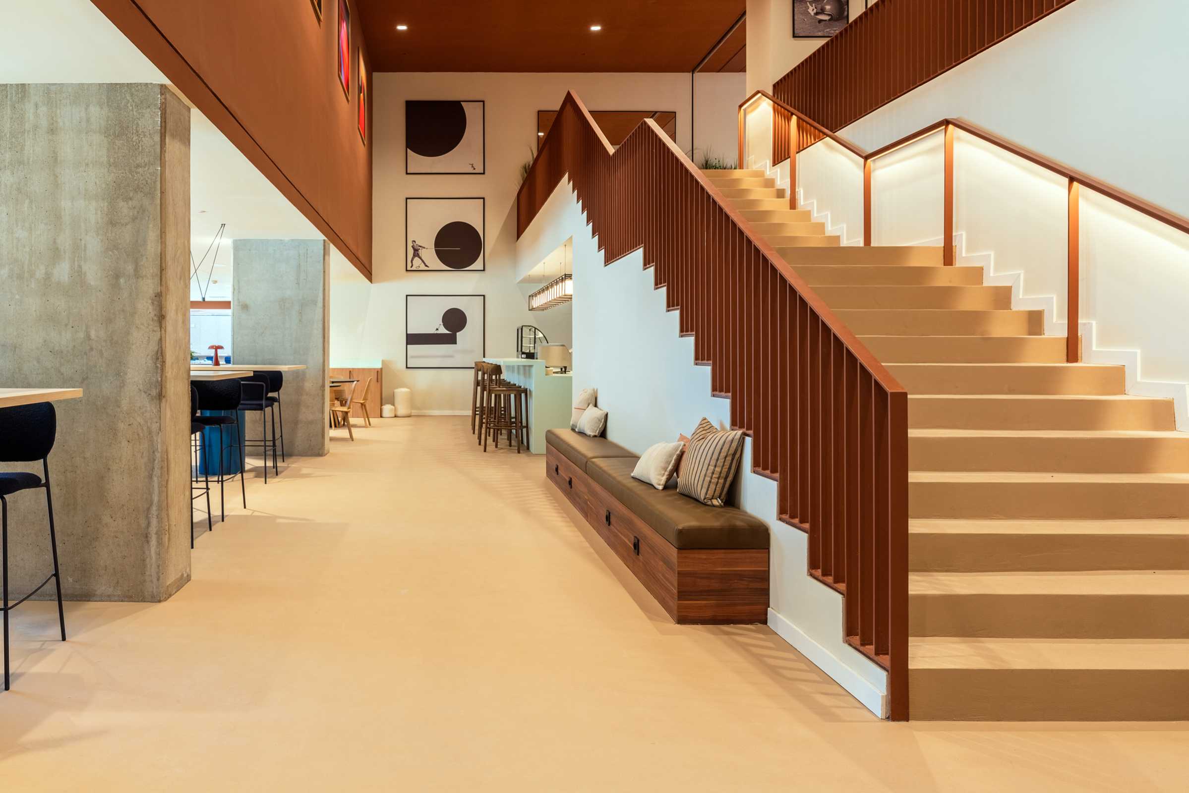 Modern interior with a wide staircase, brown railing, cushioned bench, pillows, and abstract art on the wall. Soft lighting highlights clean lines and minimalist décor.