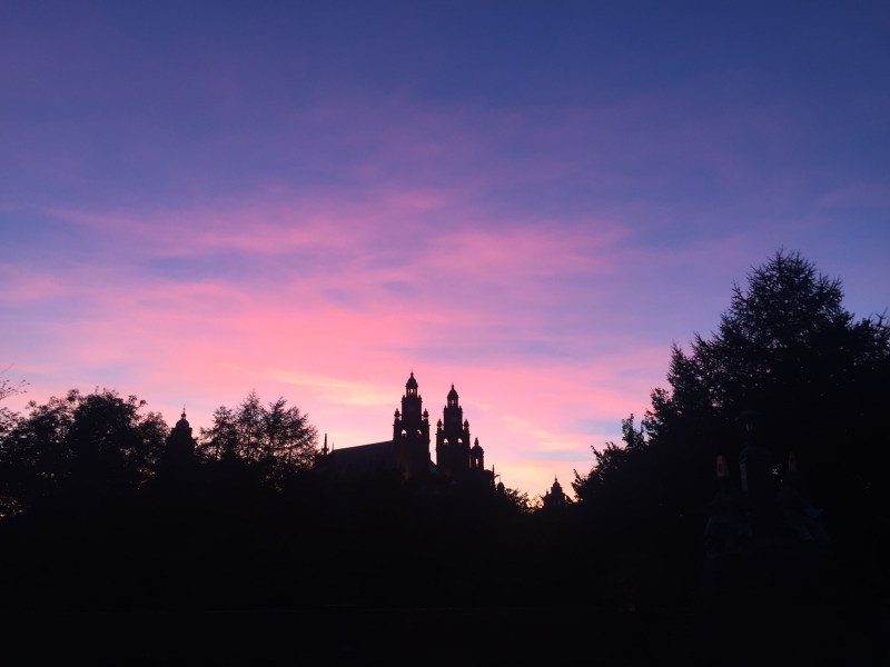 Silhouette of a building with towers and trees against a purple and pink sunset sky, capturing the vibrant atmosphere that students near West End often enjoy during evening student activities.