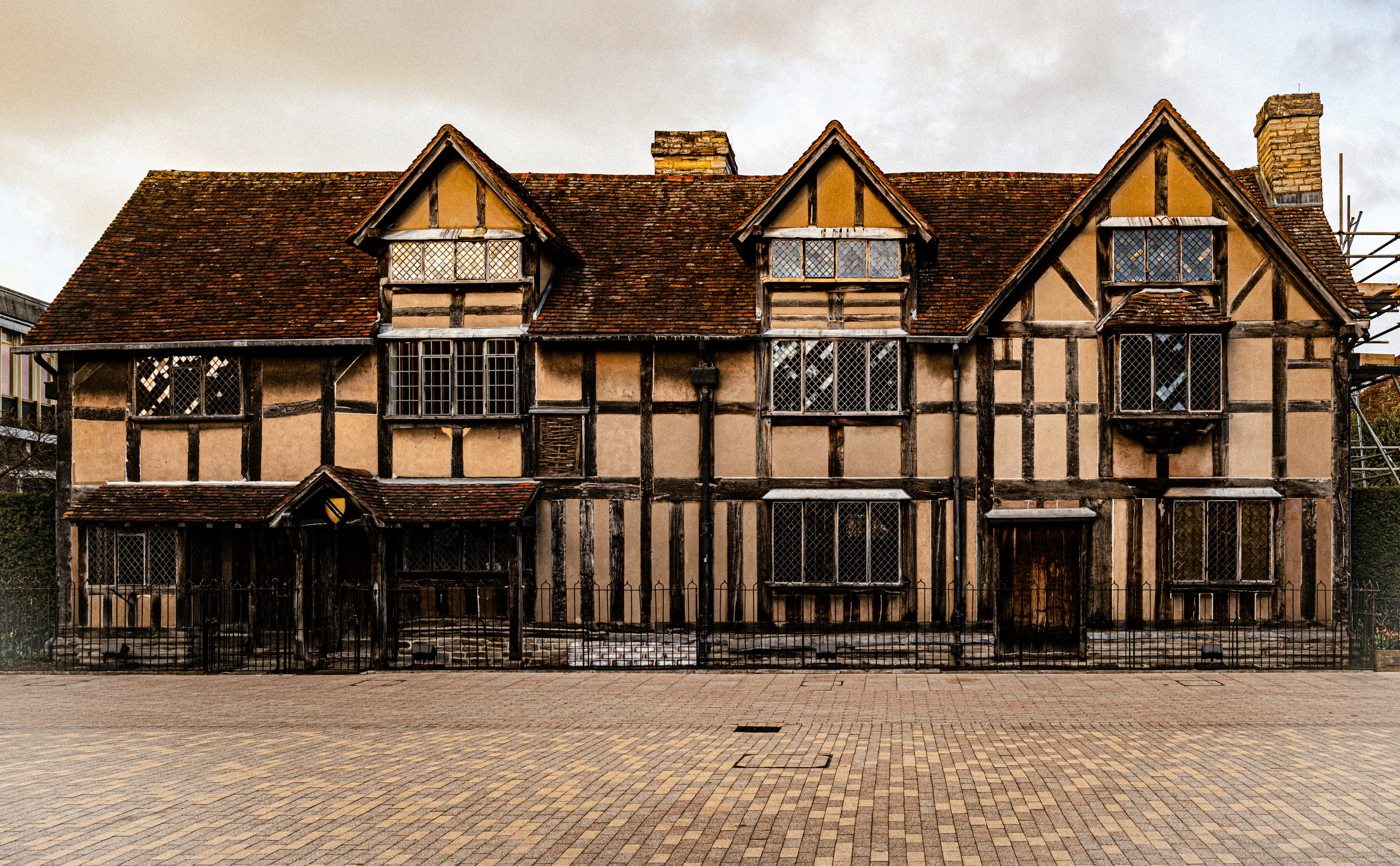 A historic Tudor-style house with timber framing, brick chimney, diamond-paned windows, and a tiled roof sits on a paved street under a cloudy sky—an inviting sight for students exploring Coventry on day trips.