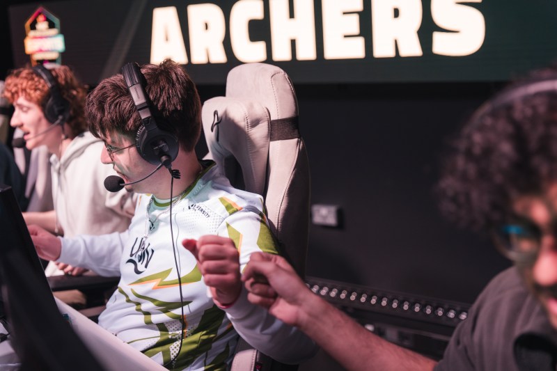 Esports players in team jerseys and headsets share a fist bump at gaming computers in front of an “ARCHERS” sign, highlighting an NSE partnership.