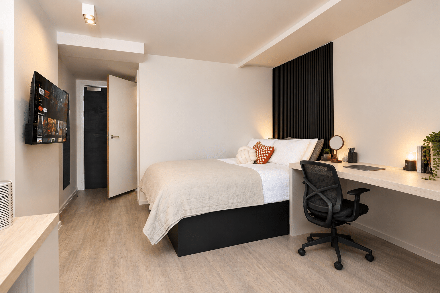 A compact bedroom with a bed, an attached desk and office chair, and a wall-mounted television.