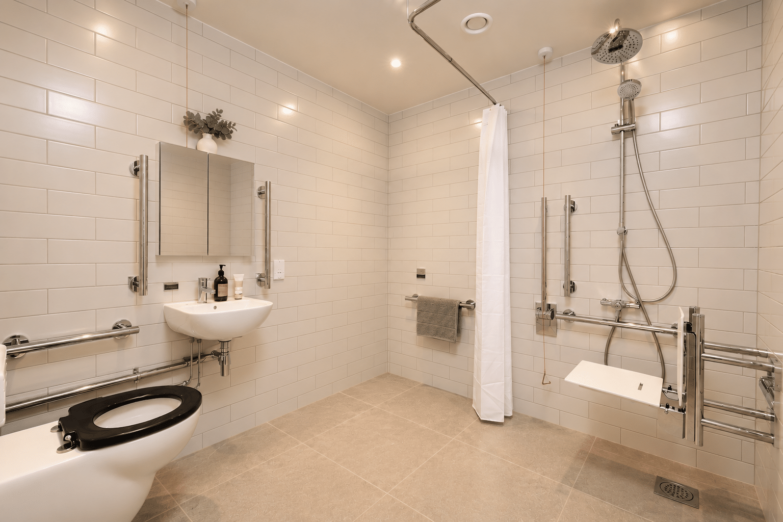 Accessible bathroom with white subway tile, a wall-mounted sink, a toilet with a black seat, and a walk-in shower area equipped with grab bars and a folding seat.