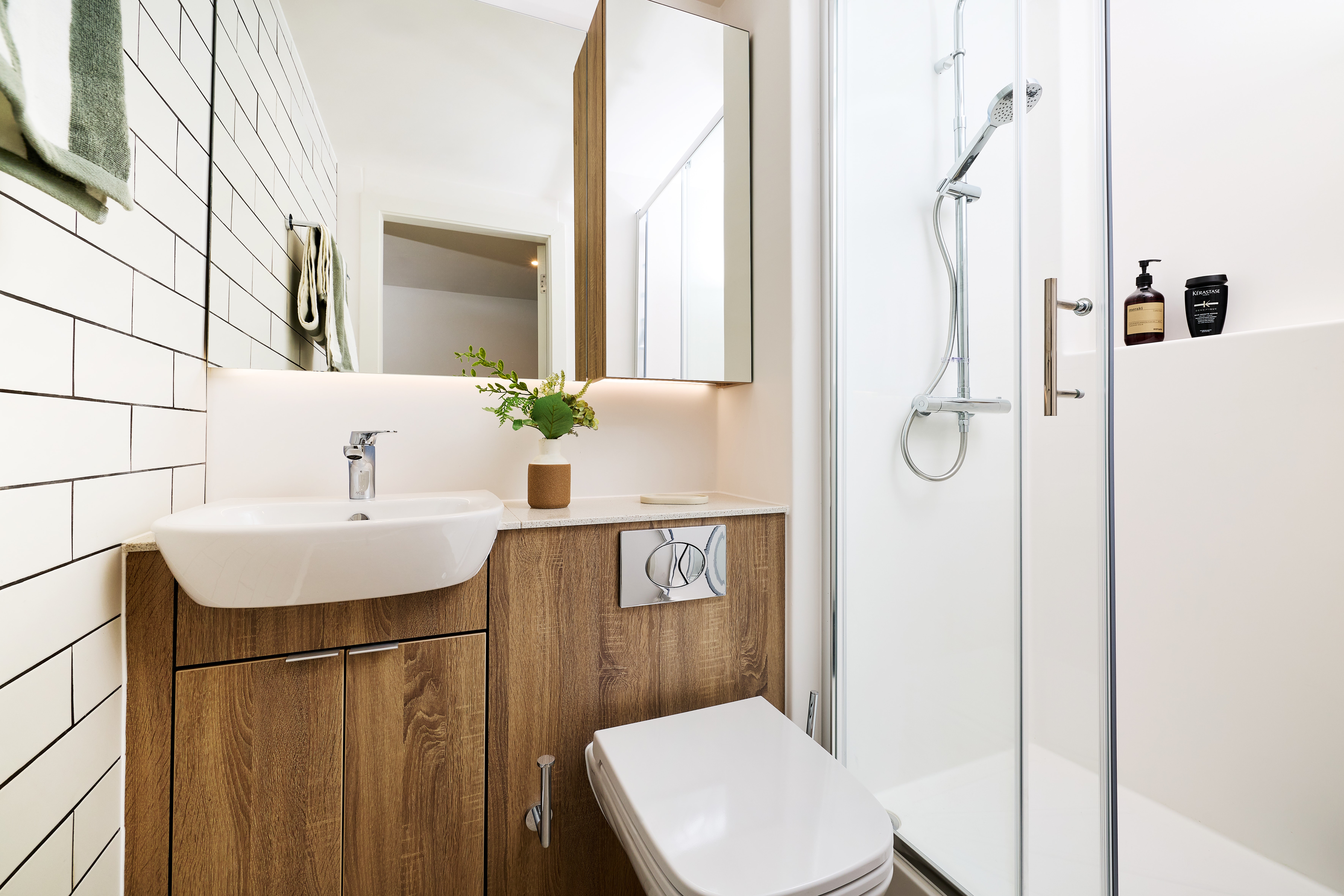 A modern bathroom featuring a white vanity sink, a wall-mounted toilet, and a glass-enclosed shower with chrome fixtures.