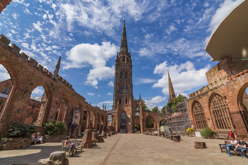 The ruins of Coventry Cathedral featuring an intact stone spire under a blue sky, situated near popular Coventry student accommodation.