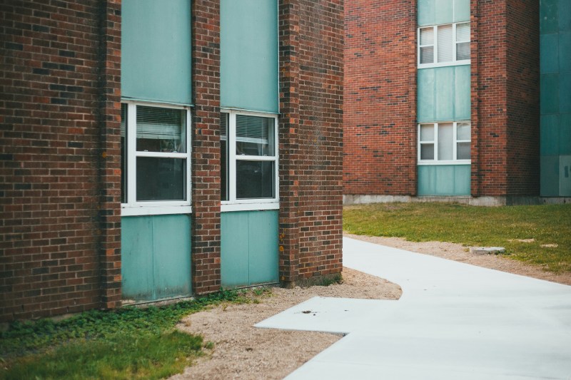 A concrete path winds between two brick student housing buildings with teal panels and white-framed windows.