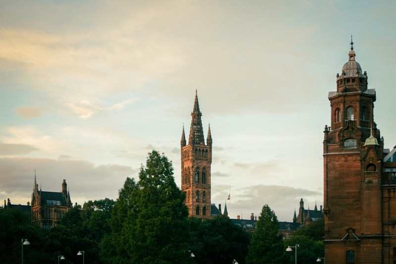 The University of Glasgow main building and its prominent clock tower rising above a park, situated near popular student accommodation in Glasgow.