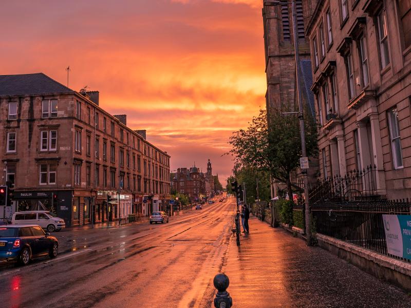 Golden sunset light reflects off the wet pavement of a historic Glasgow street, near some of the best places to live in the city.