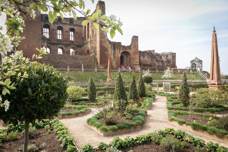 A manicured garden with shaped shrubs and gravel paths in front of the stone ruins of Kenilworth Castle, a popular destination for student travel in Birmingham.