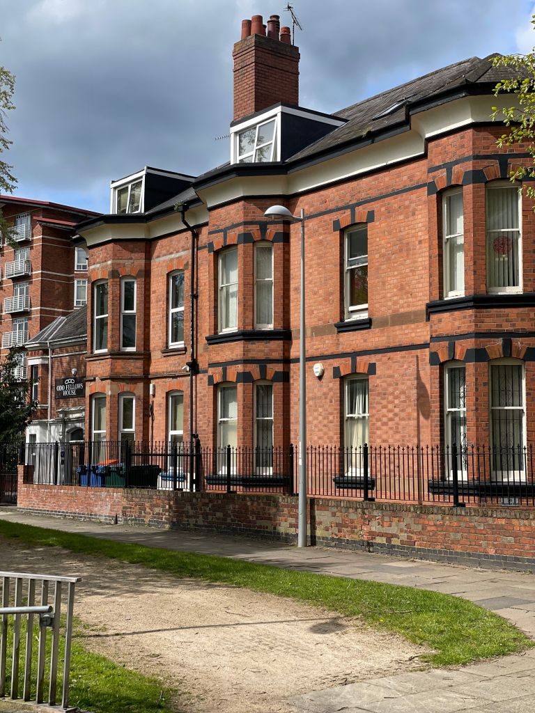 A red brick building labeled “Odd Fellows House,” popular as student accommodation in Coventry, stands behind a black metal fence along the sidewalk.
